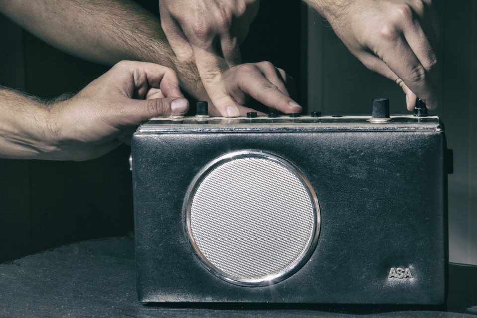 Neljä kättä säätää vanhan ASA-radion nappuloita.