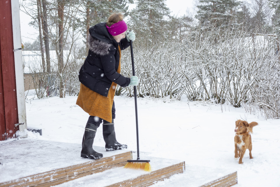 nainen harjaa lunta terasilta pois