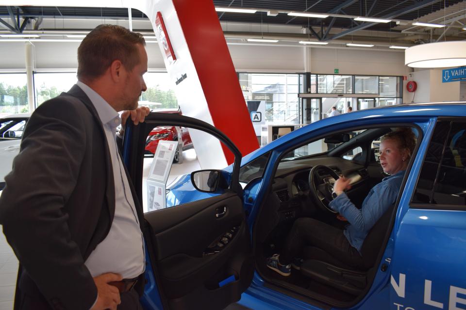 Myyntipäällikkö Sami Tuomialho esittelee Nissanin sähköautoa Anni Peltomaalle..