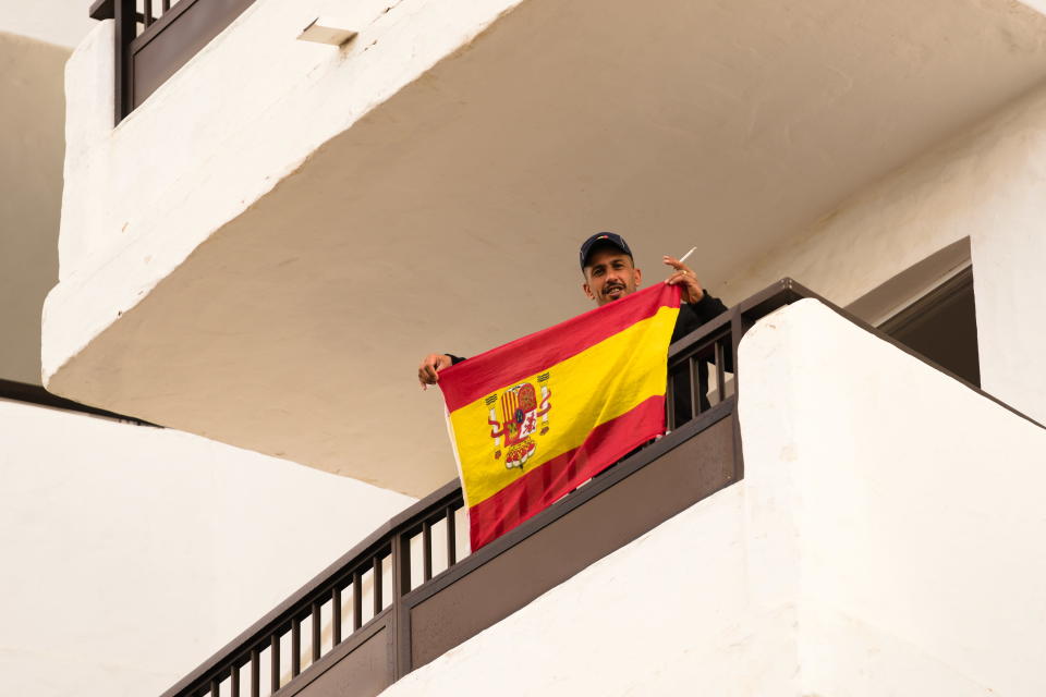 Siirtolaismies heiluttaa Espanjan lippu hotellin parvekkeella
