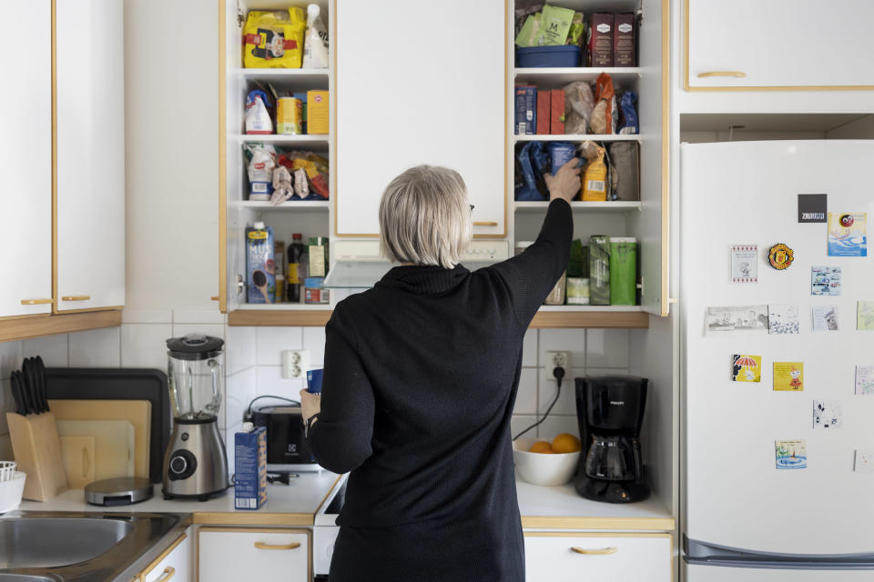 Anne Matilainen pakkaa keittiön kaappeihin ruoka-ainepakkauksia. Hänen selkänsä on kohti kameraa.