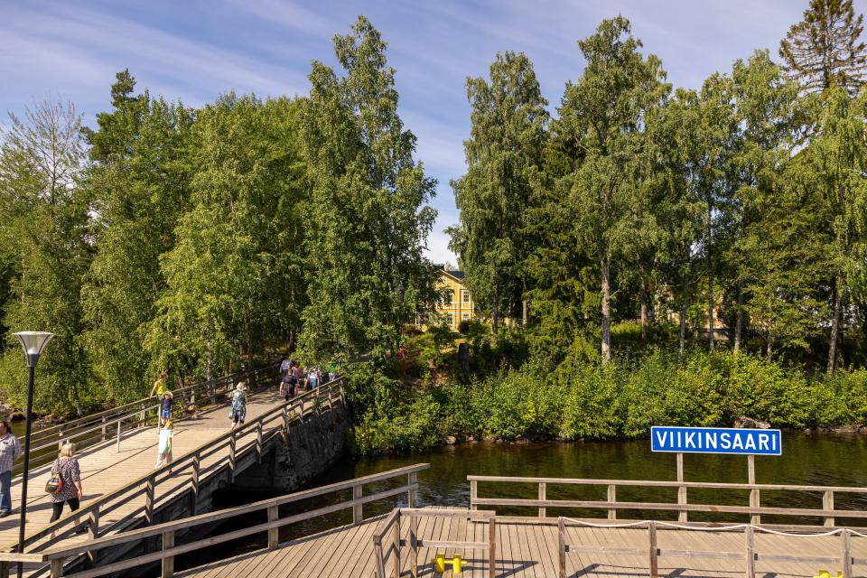 Viikinsaaren laiturialue. Etualalla laiturissa sininen Viikinsaari-kyltti, taustalla koivumetsää, joiden takaa kurkistaa puinen, keltainen päärakennus.