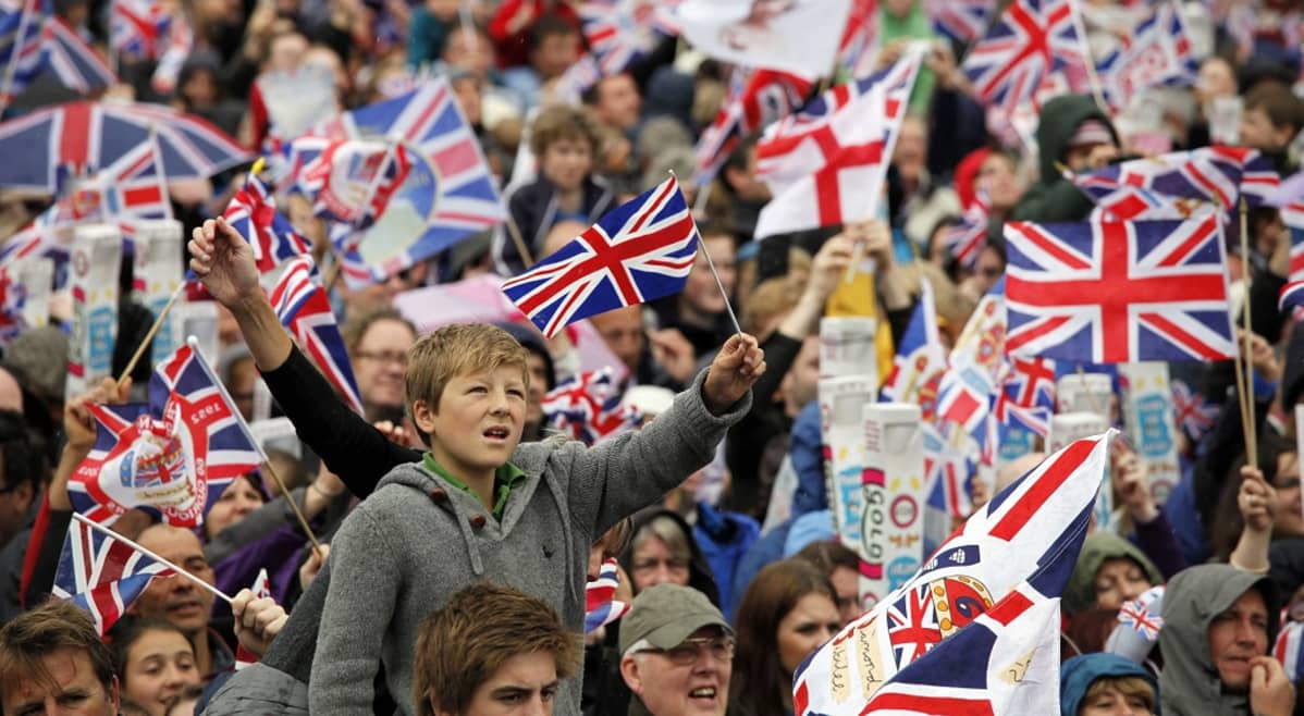 Suuri ihmisjoukko heiluttaa Britannian ja Eglannin lippuja.