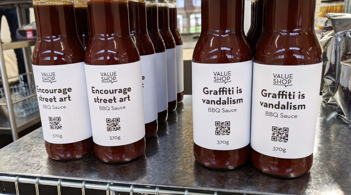 Value shop -installaation kaupassa voit ostaa tavaroita arvojesi mukaan. Hyllyssä on BBQ-kastiketta eri etiketeillä.