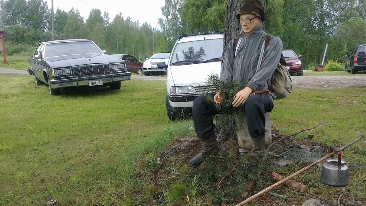 Miehen näköinen nukke nuotiokahvien äärellä Punaisen Talon pihapiirissä.