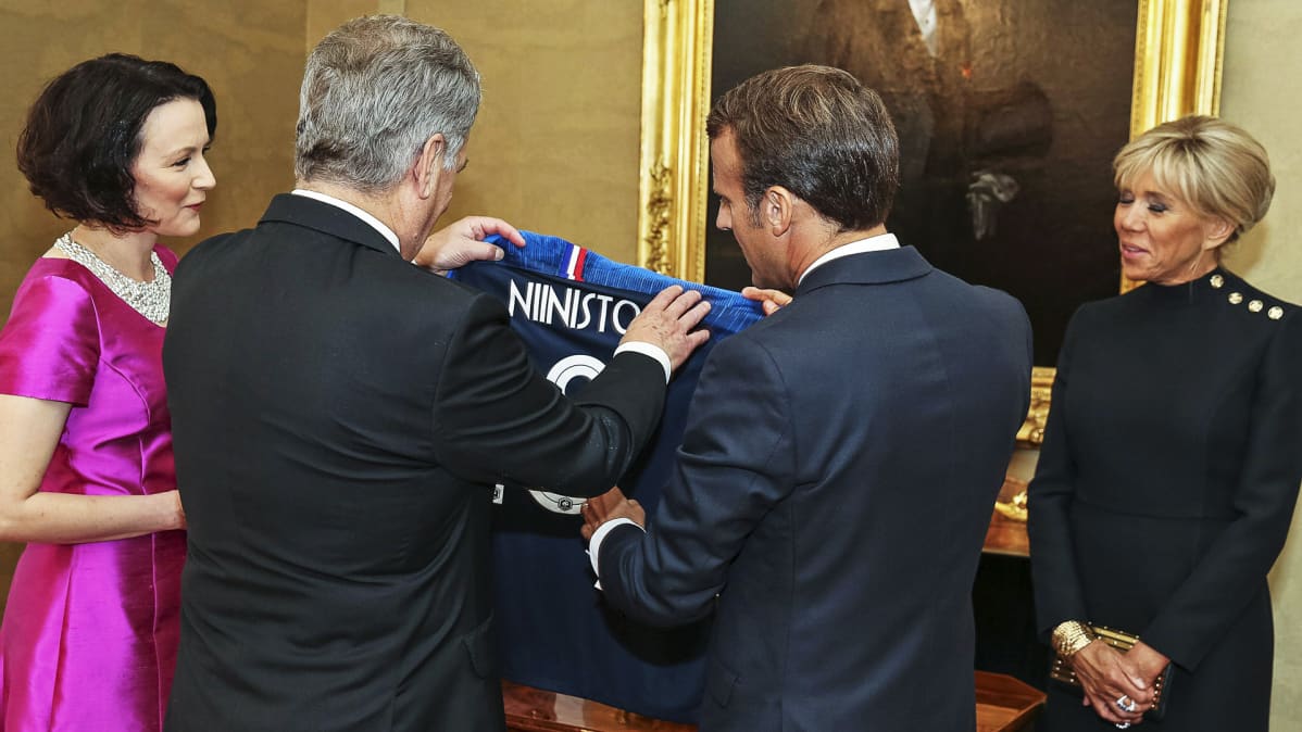 Macronit, Niinistö ja Haukio ihastelevat pelipaitaa.