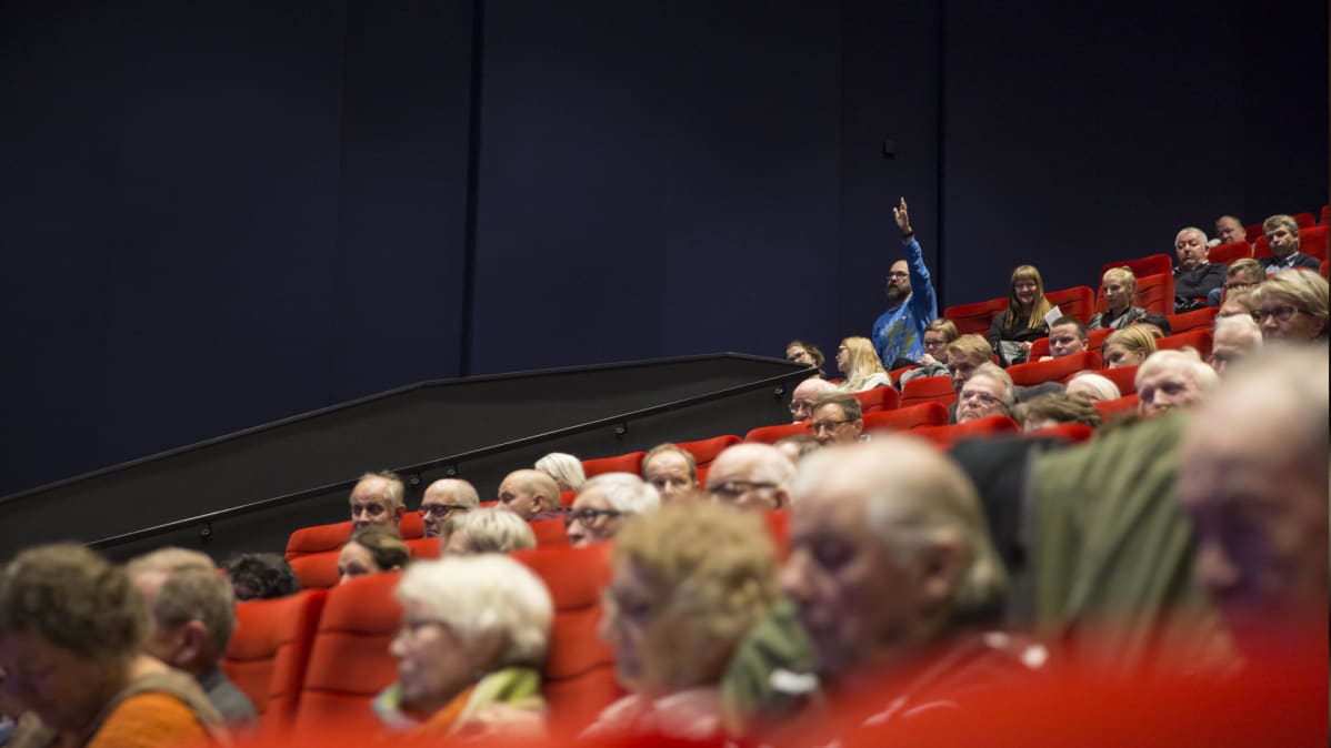 Mies viittaa yleisössä Finnpulpin tiedotustilaisuudessa.