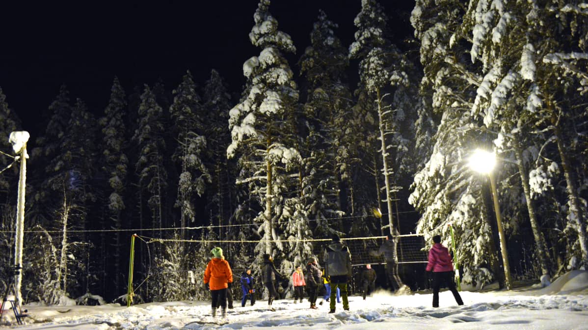 Ihmiset pelaamassa lentopalloa talvella ulkona.