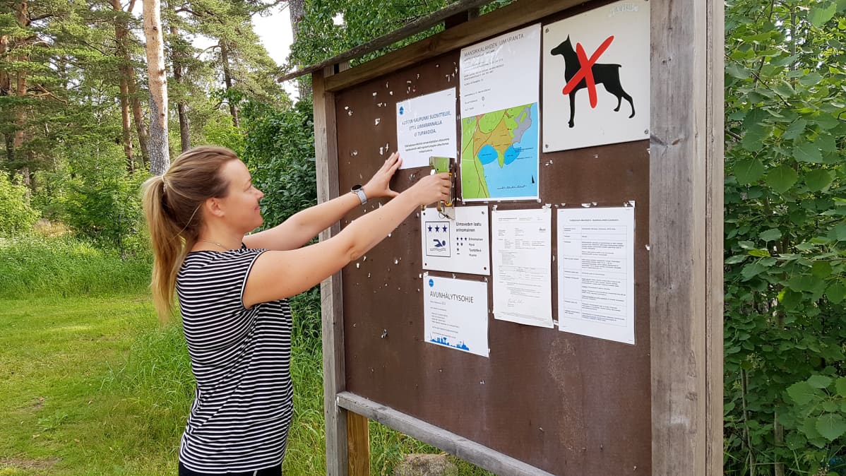 Nainen kiinnittää uimarannalle lapun rannan savuttomuudesta