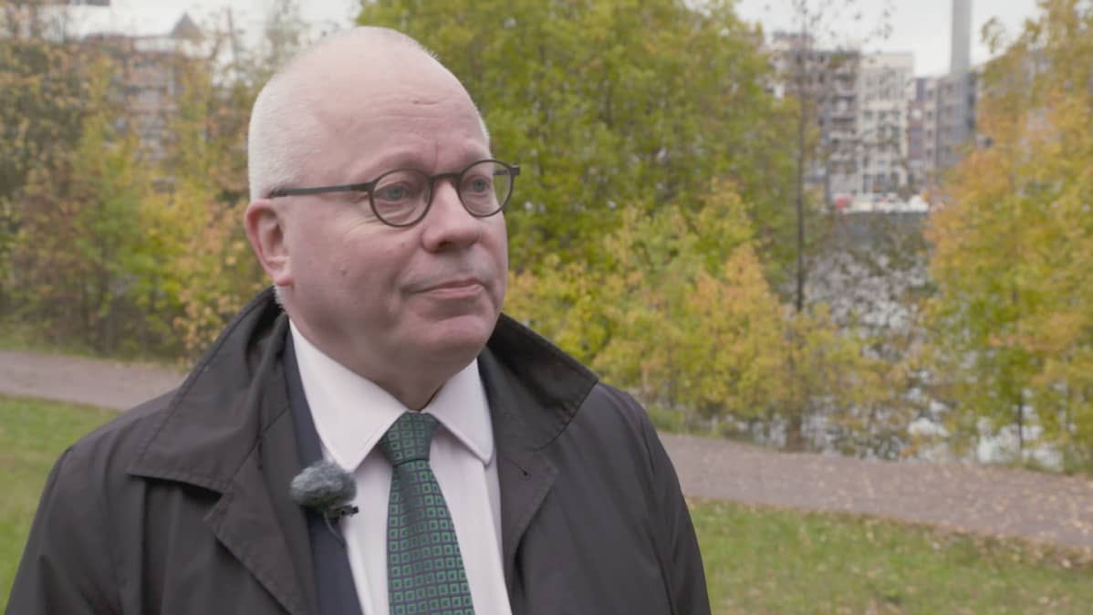 Pukumies seisoo ruskapuiden edessä.