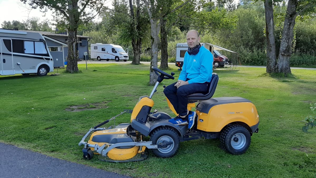 Kuvassa mies istuu ruohonleikkurin päällä.