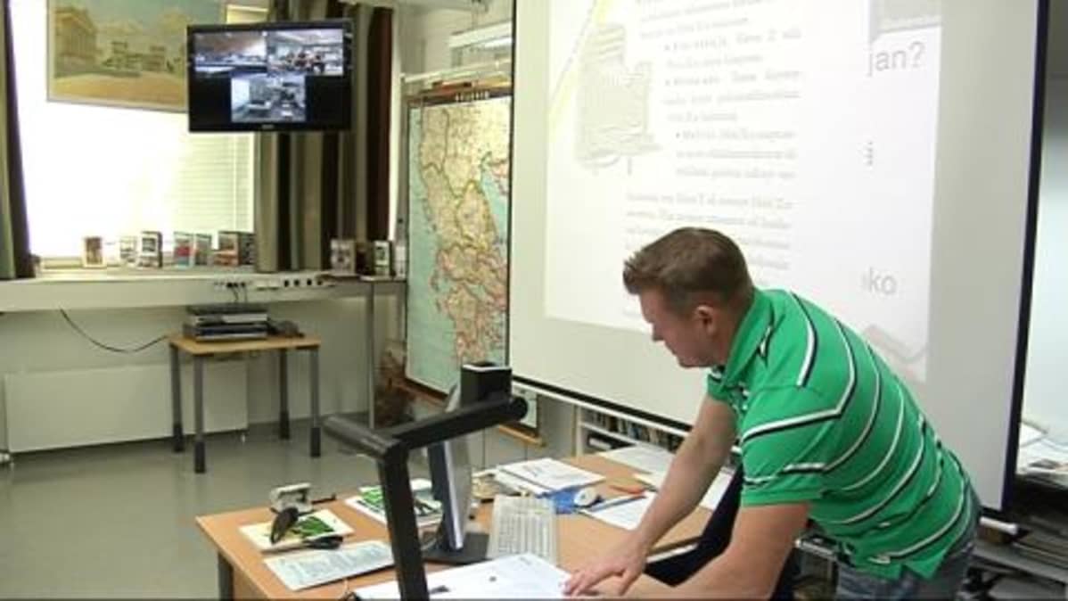 Opettaja opettaa kolmen lukion oppilaita video-yhteyden avulla.