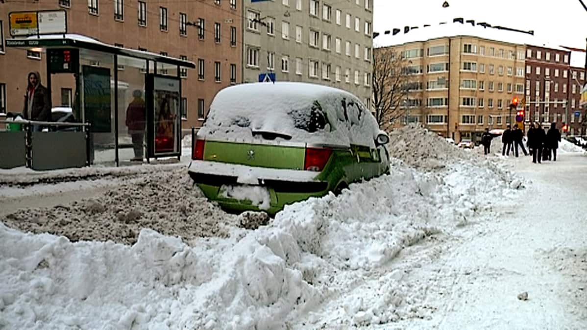 Henkilöauto on jäänyt kadun reunaan, lumivallien väliin.