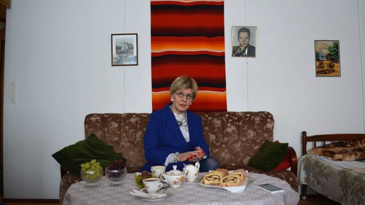 Ensio Nyman, Eveliina, istuu olohuoneessaan sohvalla, edessä pöydällä kahvikattaus.