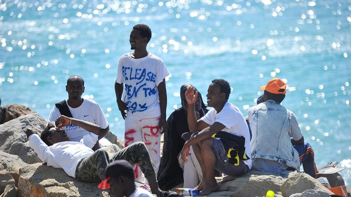 Pakolaisia aurinkoisilla rantakivillä.