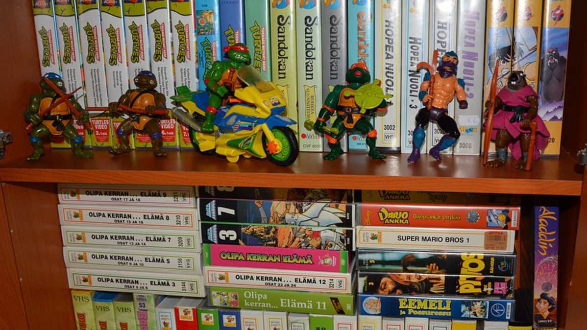 Hyllyssä Turtles-lelufiguureja sekä vhs-kasetteja.