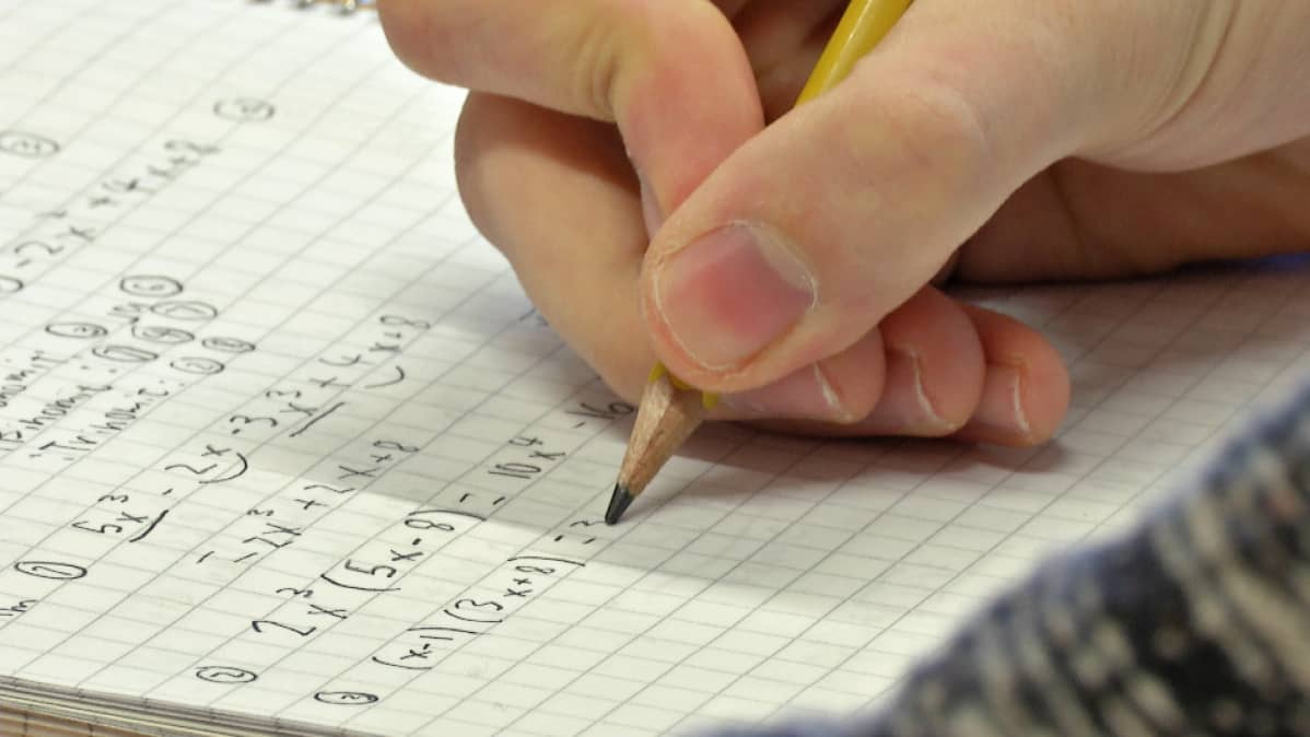 Oppilas kirjoittaa matematiikan tehtävää vihkoon