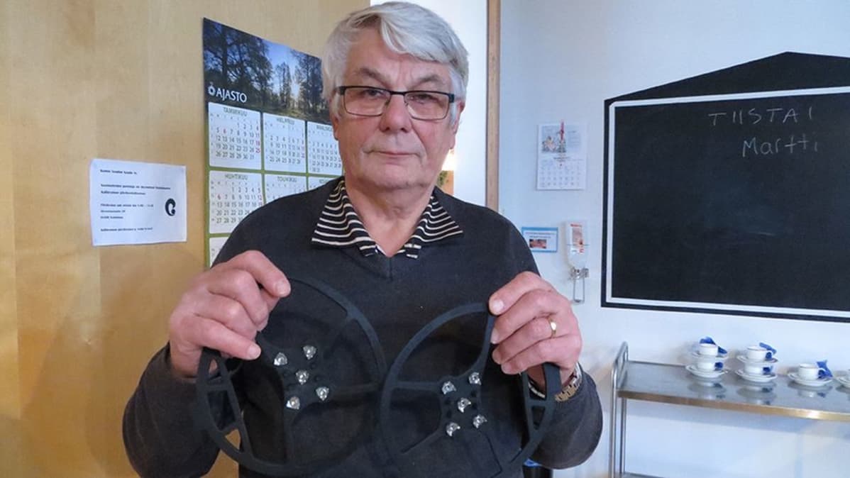 Keminmaan vanhusneuvoston puheenjohtaja Lasse Vaaraniemi kädessään kenkien liukuesteitä.