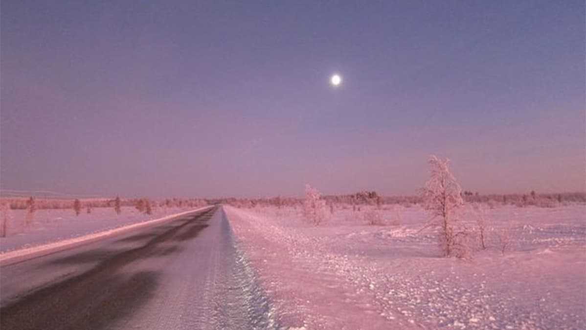 Maantie halkoo lumista, punertavaa maisemaa.