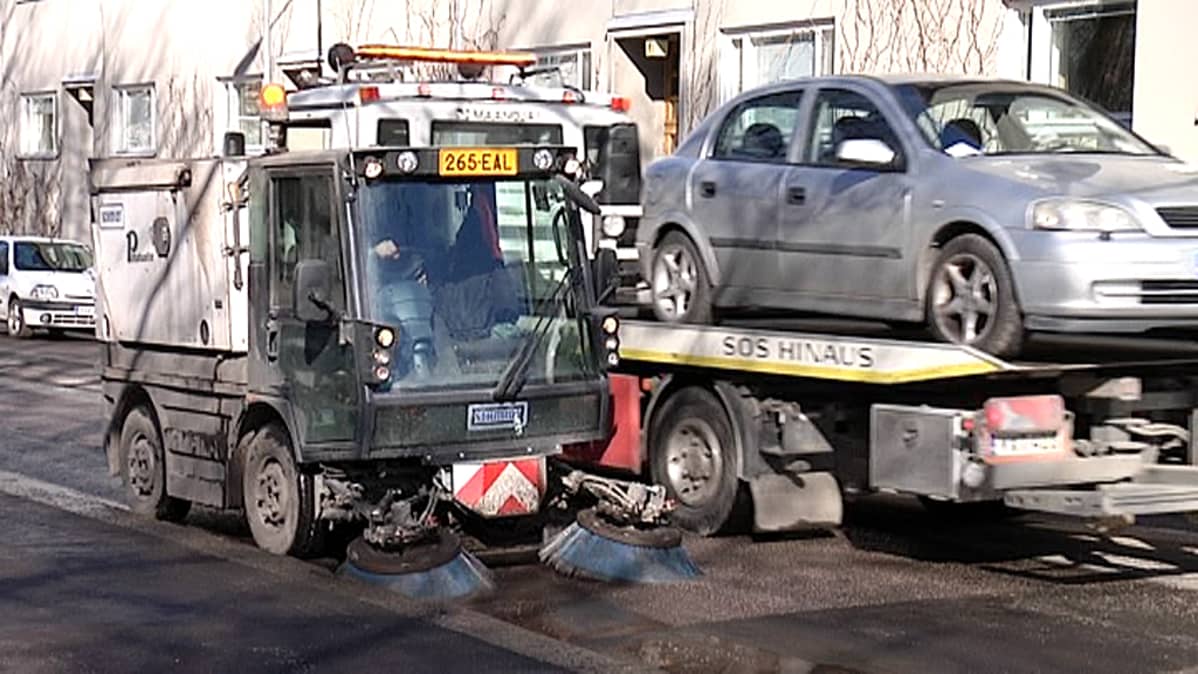 Harjakone siivoaa katua ja hinausauto siirtää henkilöautoa