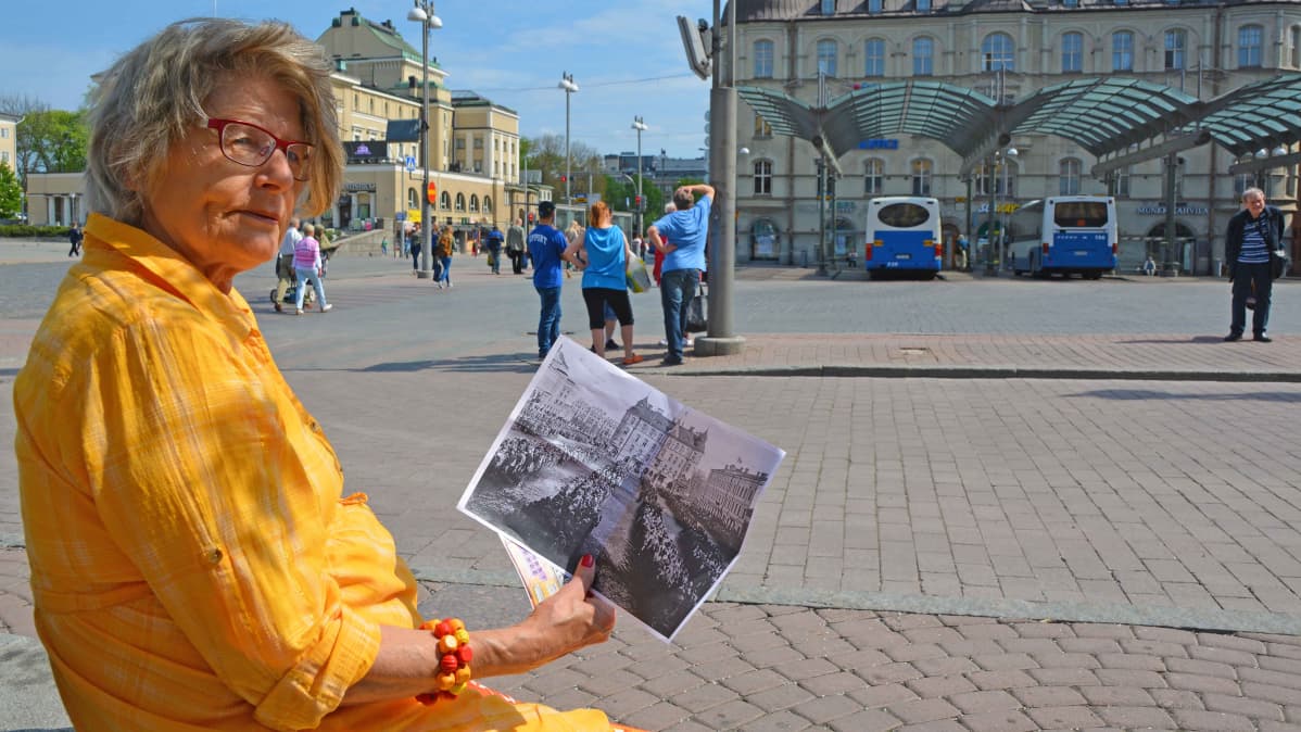 Merja Pikkola istuu Keskustorin penkillä ja katsoo sodanaikaista kuvaa torista.