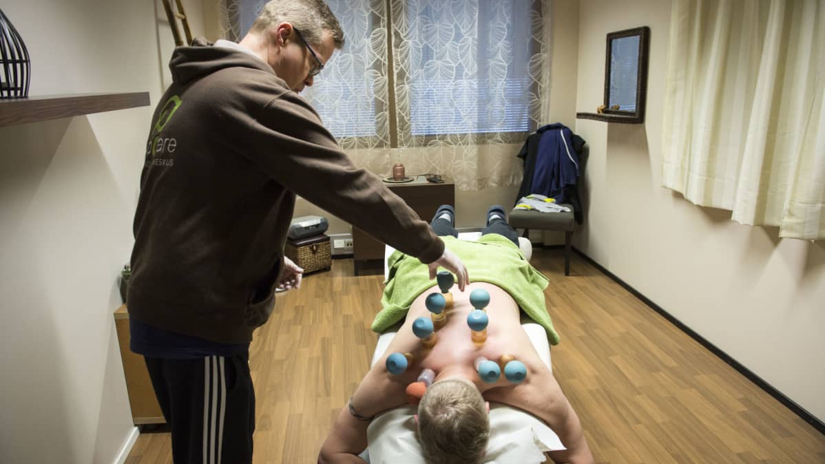 Fysioterapeutti Pekka Mykkänen tekee kuppausta hierontapöydällä makaavalle asiakkaalle.