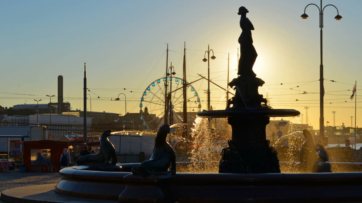 Havis Amanda -patsas kuvattuna nousevaa aurinkoa vasten. Taustalla Helsingin Kauppatori.