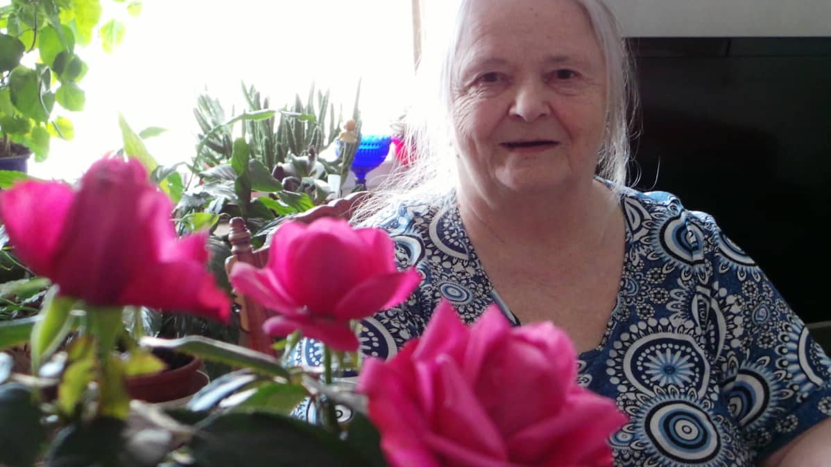 Marja-Liisa Isoviita hymyilee ruusujen takana.