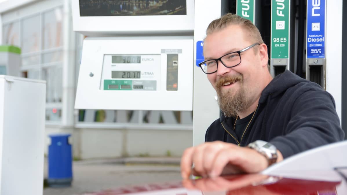 Antti Heikkinen tankkaa autoa ja hymyilee.