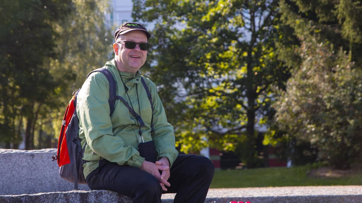 Veli Huovinen istuu ulkona ja hymyilee.
