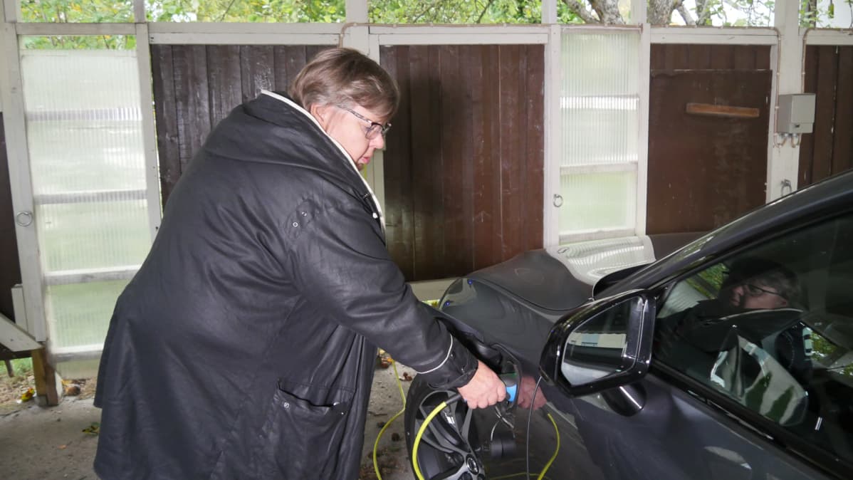Tuula Toivakka kytkemässä sähköauton kaapelia autoonsa.