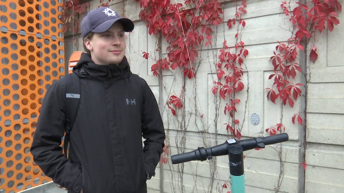 Nuori opiskelija Paavo seisoo Vaasan ammattikorkeakoulun pääovenb edustalla. Saapui juuri sähköpotkulaudalla luennolle.