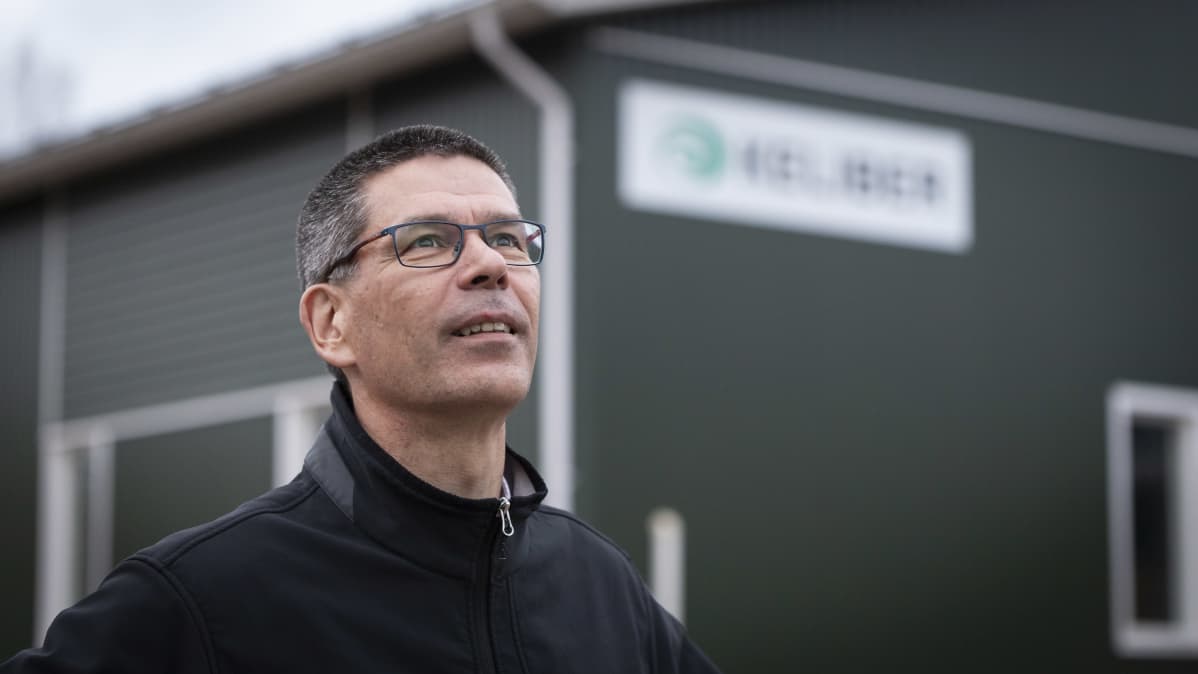 Hannu Hautala lähikuvassa vihreän rakennuksen edessä. Katselee kaukaisuuteen.