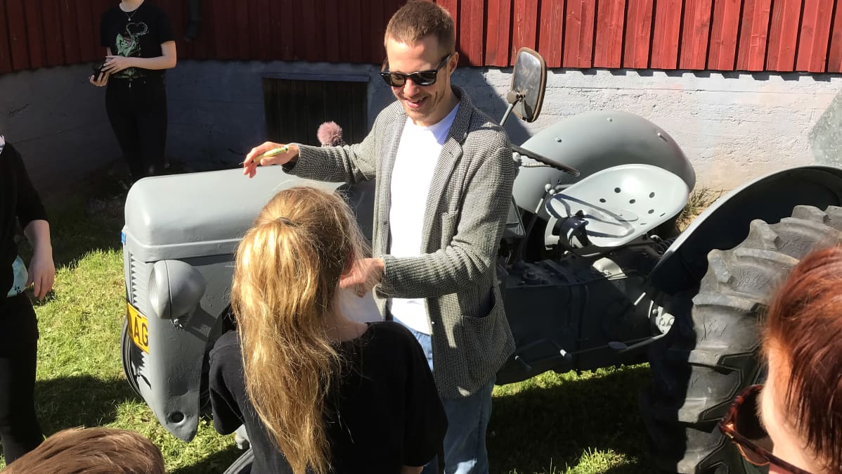 Olavi Uusivirta traktorin vieressä jakamassa nimmareita koululaisille