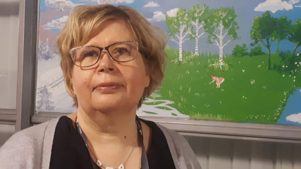Vaalea, silmälasipäinen nainen katsoo kameraan