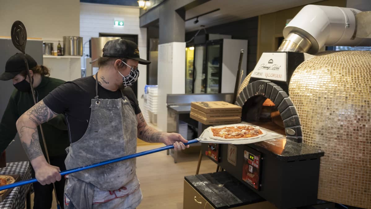 Mies laittamassa pizzaa uuniin.