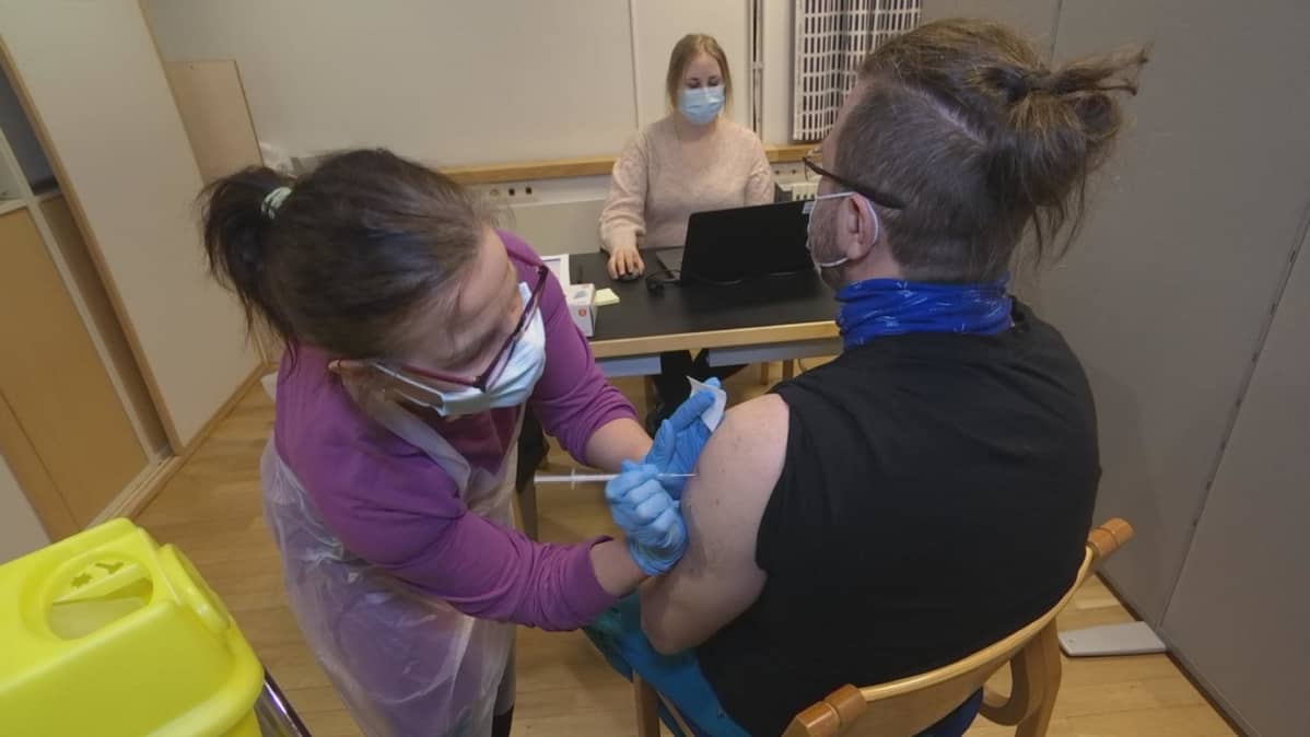 Riitta Iivari antaa koronarokotetta Mauri Määtäle. Sara Tiirola kirjaa tiedot talteen.
