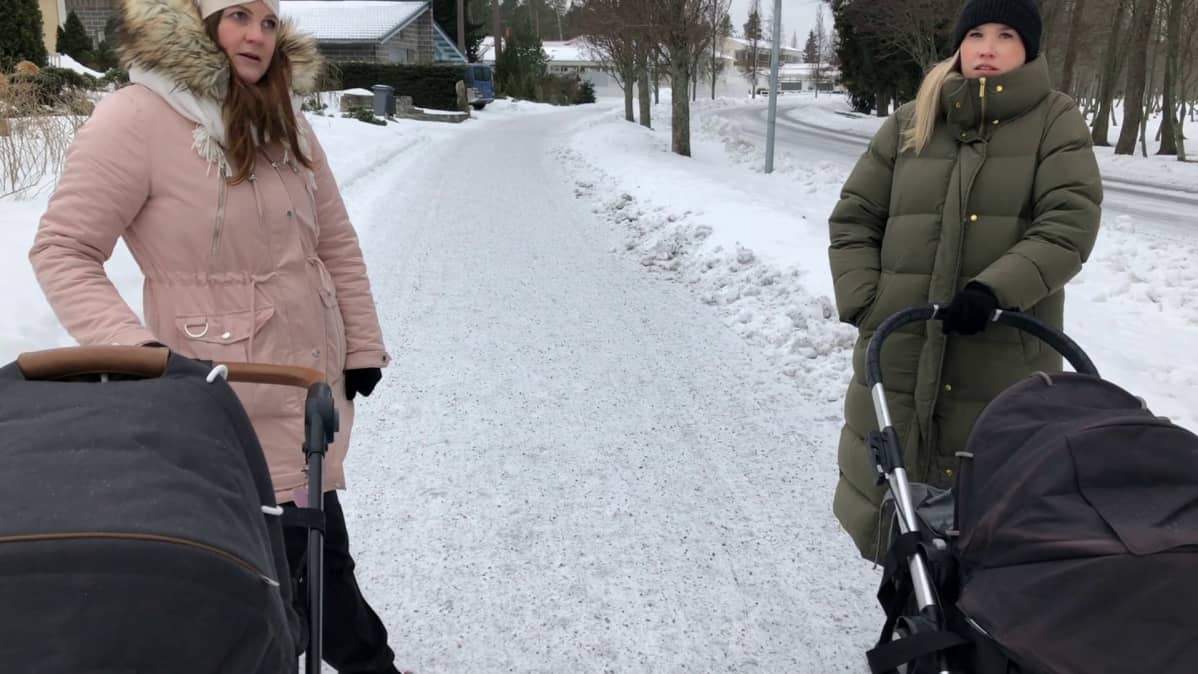 Naiset juttelevat lastenrattaiden kanssa lumisella jalkakäytävällä