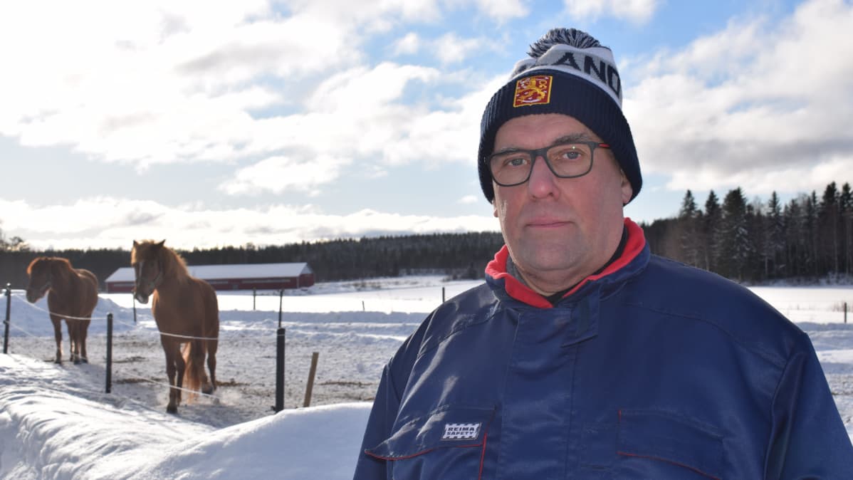 Kankaanpään seudun tykistökillan puheenjohtaja Kimmo Tuomi seisoo ulkona talvella kaksi hevosta seisoo taustalla syömössä