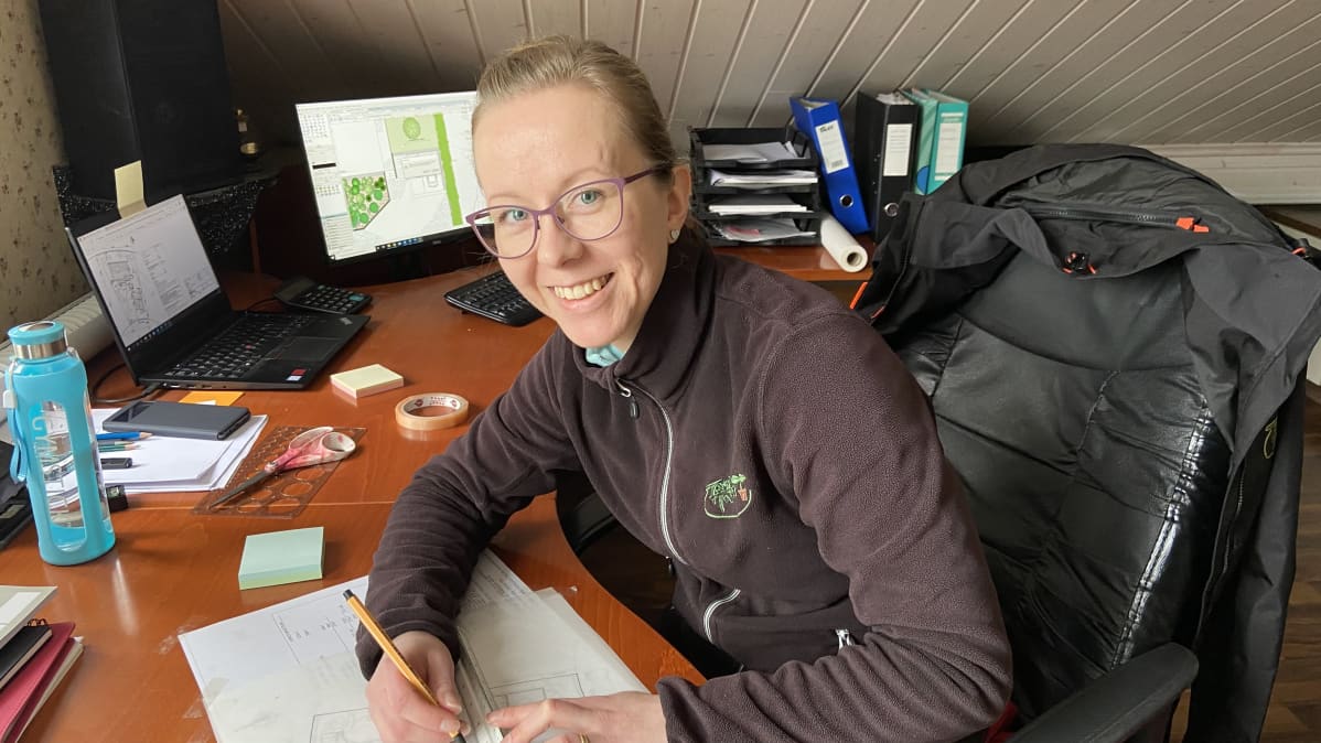 Kuvassa suunnitteluhortonomi Anna-Maija Furu työpöytänsä ääressä piirtämässä pihasuunnitelmaa.