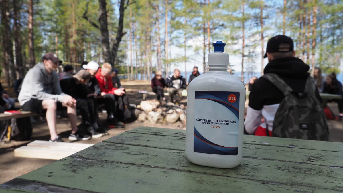 Koronakevään rippileiriläiset istuskelevat ringissä, etualalla käsidesipullo