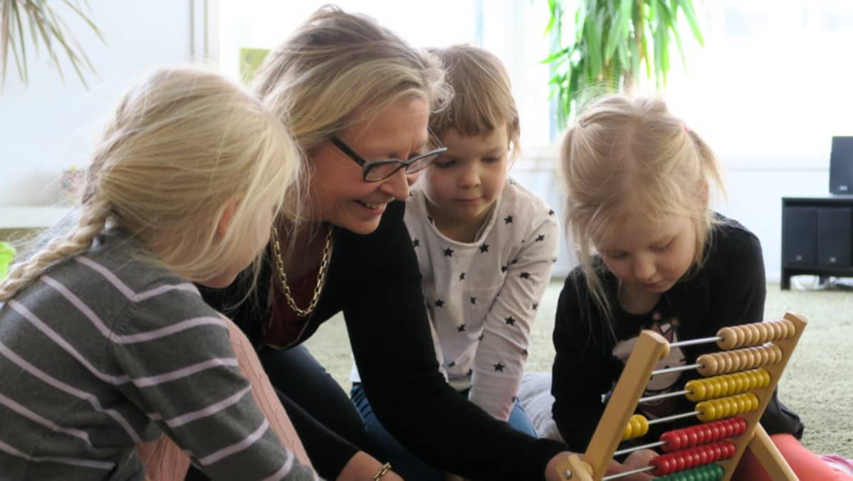 Sari Louhio-Järvinen leikkii kolmen tytön kanssa helmitaululla