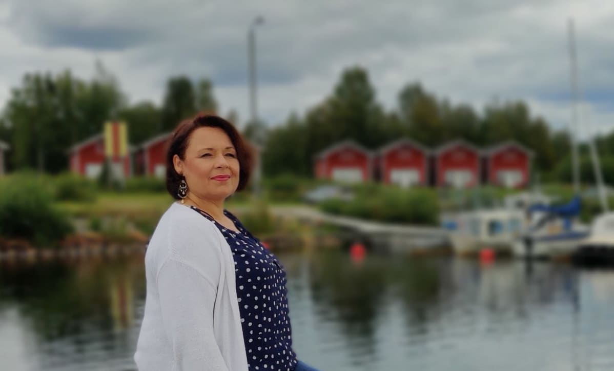 Oopperalaulaja Tuija Knihtilä Simon venesatamassa, taustalla aittarakennuksia.