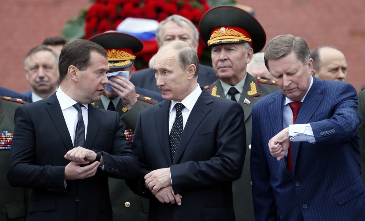 Venäjän pääministeri Dimitri Medvedev (vas.), presidentti Vladimir Putin ja hallintopäällikkö Sergei Ivanov (oik.) vierekkäin tutkimassa kellojaan. Taustalla sotilashenkilöitä.