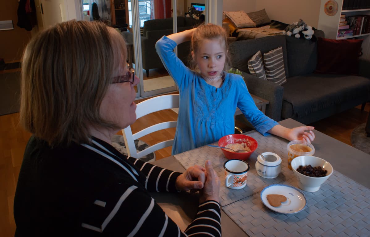 Seija Vahvelainen istuu tyttärentyttärensä kanssa ruokapöydässä.