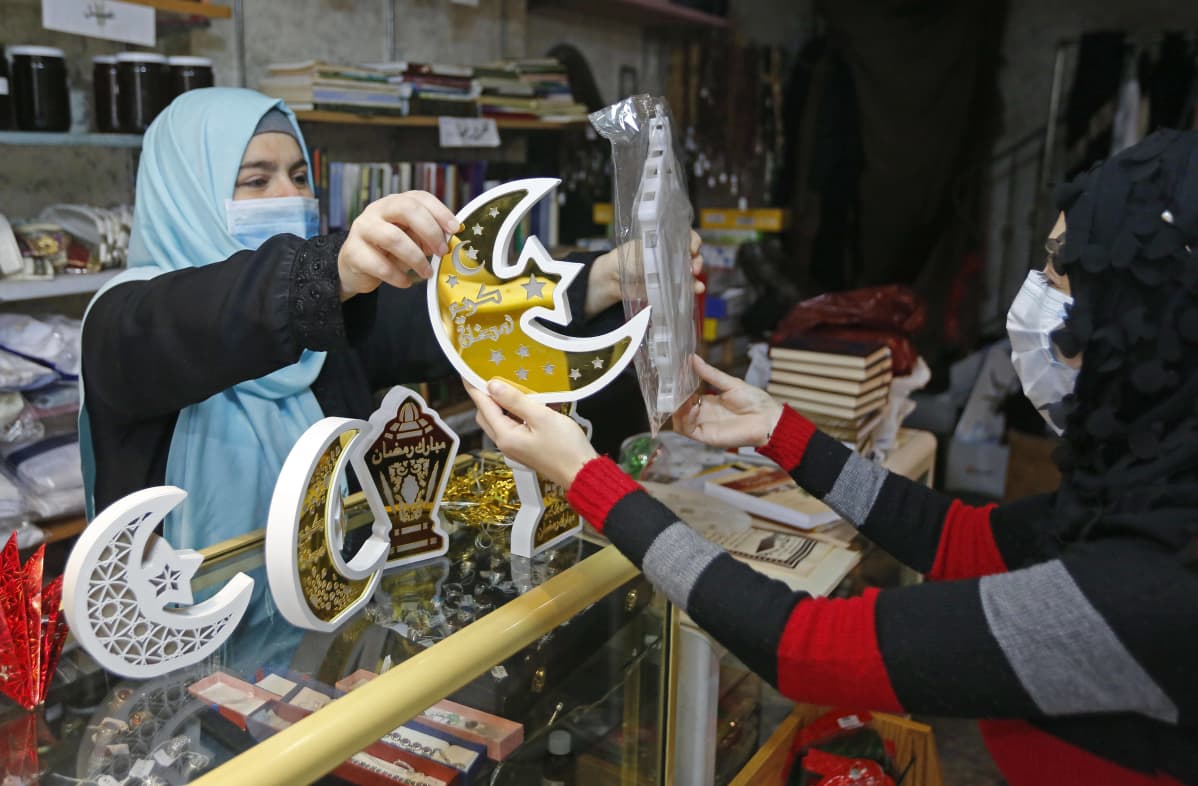 Kaksi hengityssuojaimin suojautunutta naista sekä kuunsirppejä esittäviä koristeita.