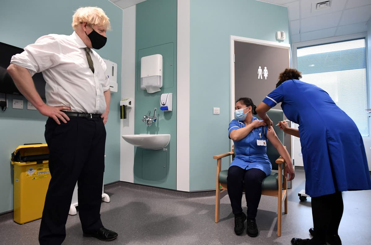 Britannian pääministeri Boris Johnson seuraa kun sairaanhoitaja rokottaa toisen sairaanhoitajan.