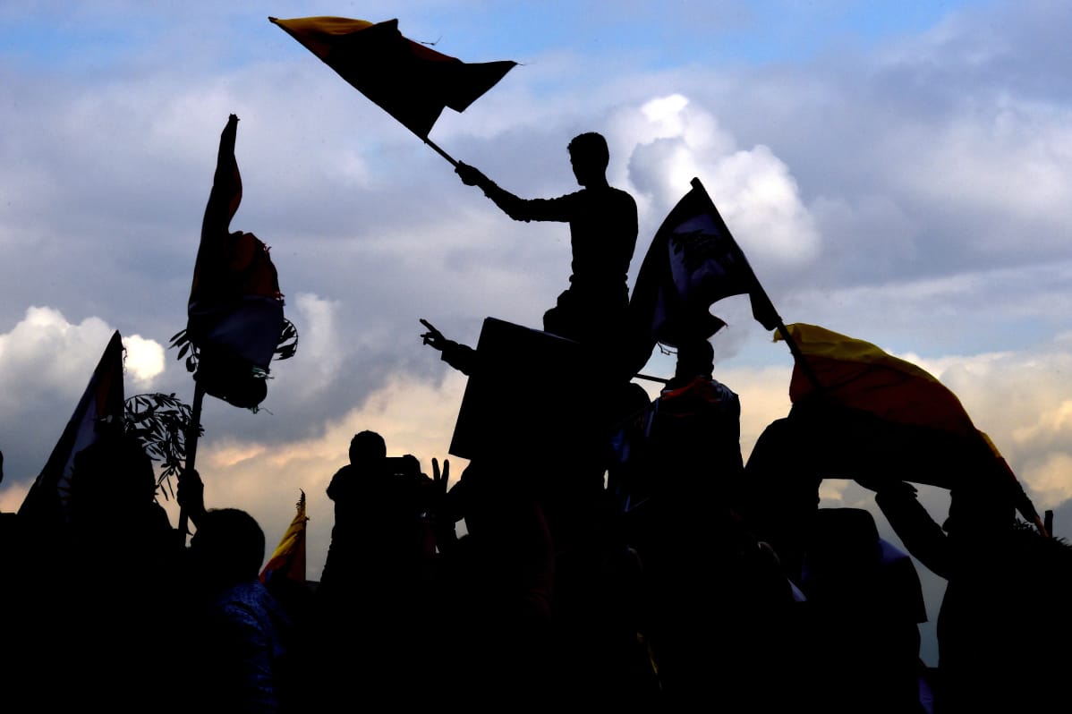 Silhuetissa kurdilippuja heiluttavia mielenosoittajia