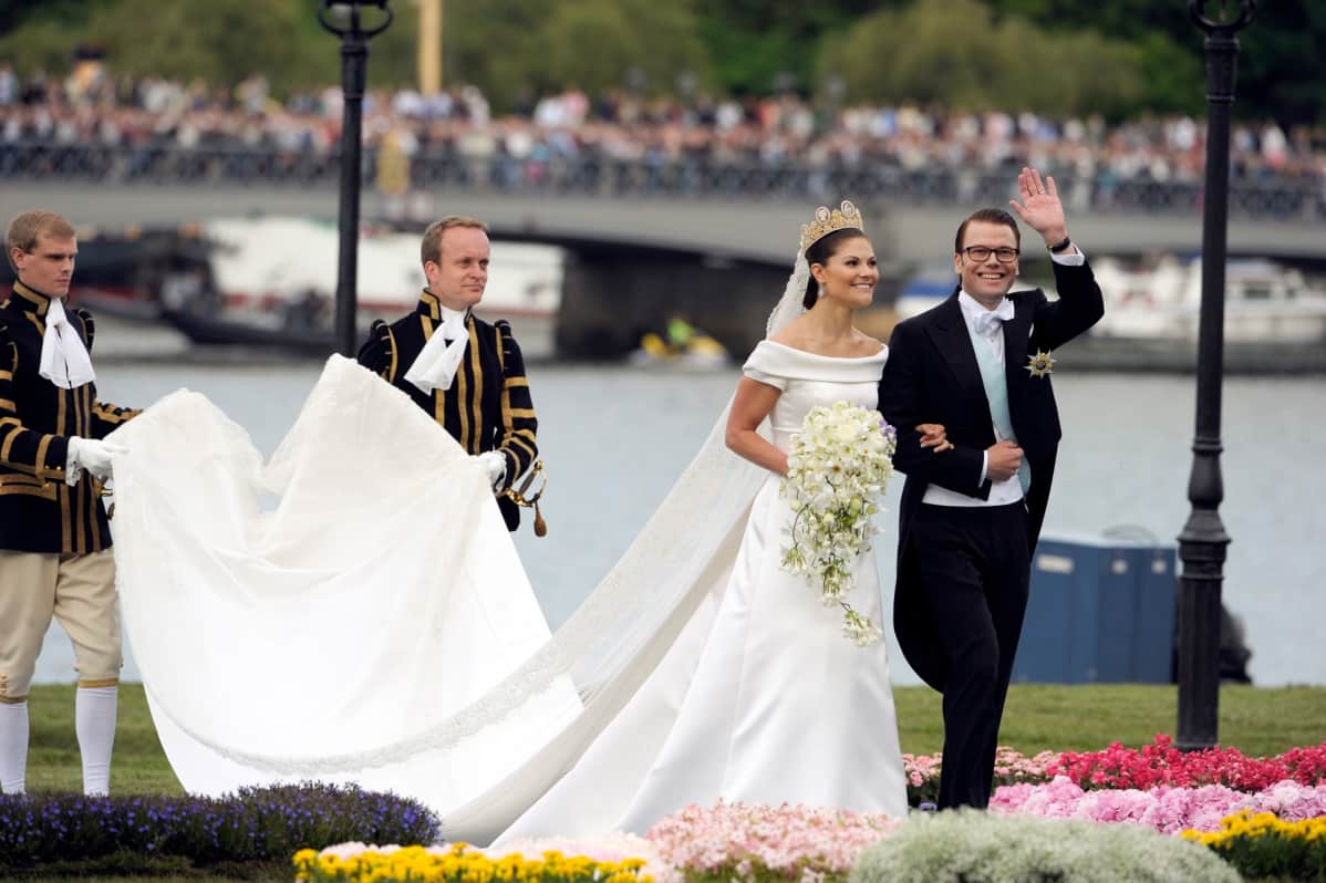 Victoria ja Daniel Kuninkaanlinnan rannassa, perässä kaksi miestä kantaa Victorian laahusta.
