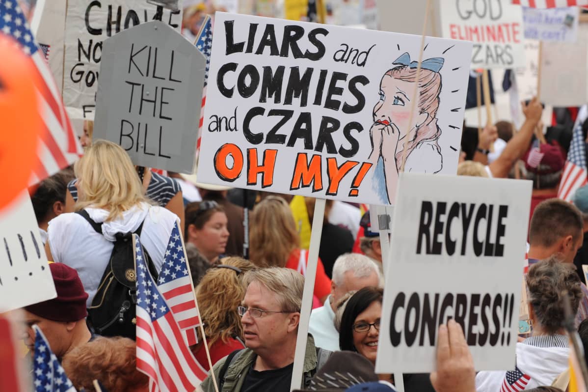 Mielenosoittajia teekutsuliikkeen tilaisuudessa, kyltissä lukee englanniksi: Liars commies and Czars, Oh my".